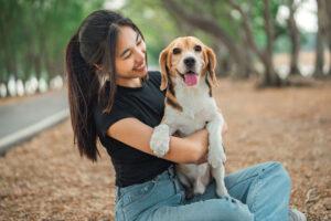 woman smiling and holding a Beagle outside at the park